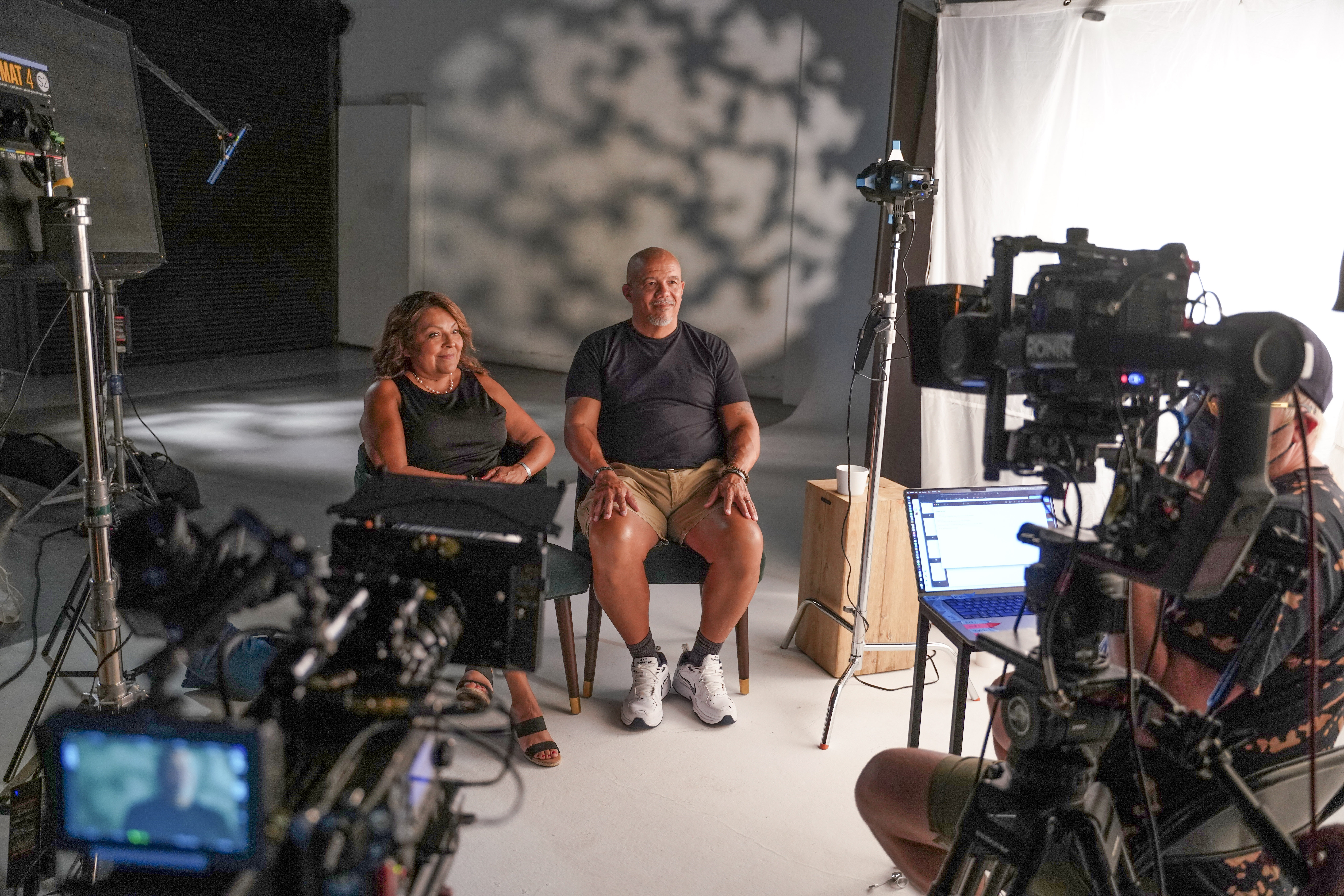 Man and woman sit facing camera on video set 