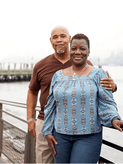 middle aged couple standing in an outdoor pathway with a body of water in the background